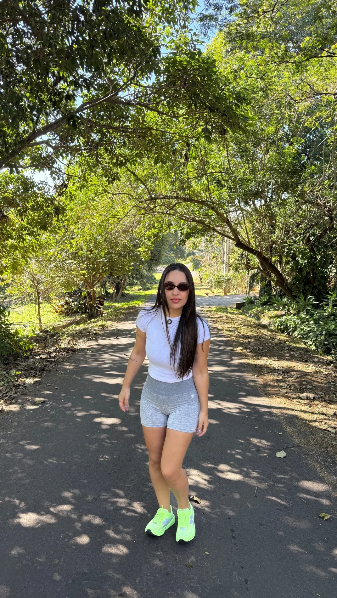 Vanessa Reis de óculos escuros caminhando por uma trilha arborizada em um parque