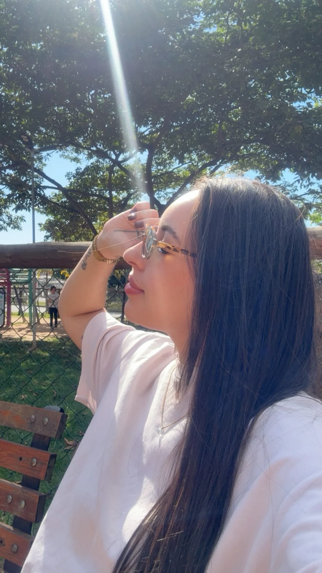 Vanessa Reis de perfil, com óculos, sob a luz do sol em um parque
