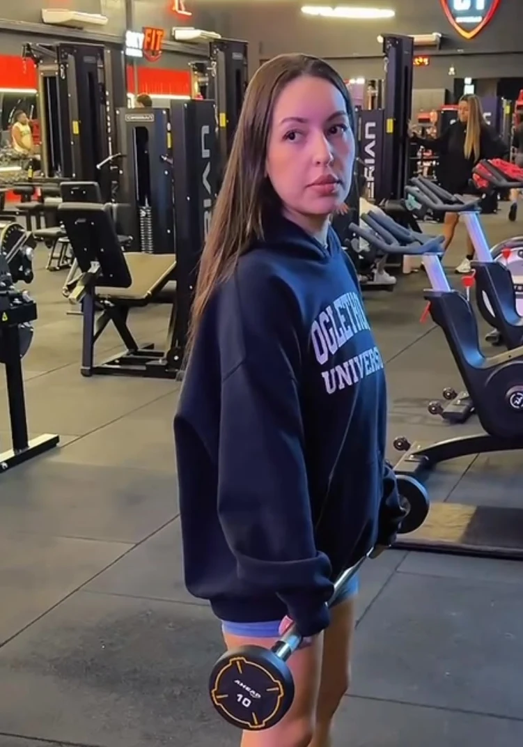 Vanessa Reis de moletom em uma academia, segurando um halter durante a rotina de treino